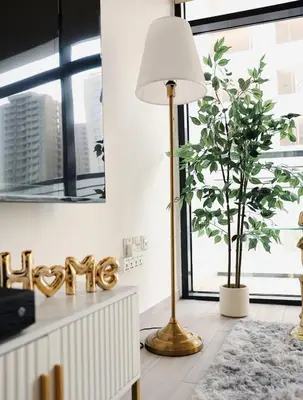 a gold floor lamp in a living room with a plant at Elegant Studio with Pool & Gym in JVC in Dubai