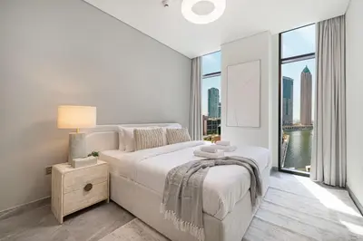 a white bedroom with a bed and a large window at StayMada - Peninsula Panoramic Waterfront Views in Dubai