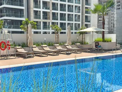 a pool with chairs and umbrellas next to a building at Modern Retreat at Azizi Azure, Meydan in Dubai