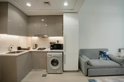 a kitchen with a washing machine and a couch at Azizi Modern Studio 10 min to Downtown in Dubai