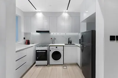 a white kitchen with a washing machine and a refrigerator at Elegant 1BR Stay in Binghatti Heights JVC in Dubai
