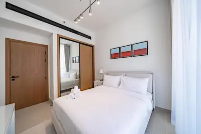 a white bedroom with a large bed and a mirror at Homes Beyond l 1BR Cozy Modern Escape in JVC in Dubai