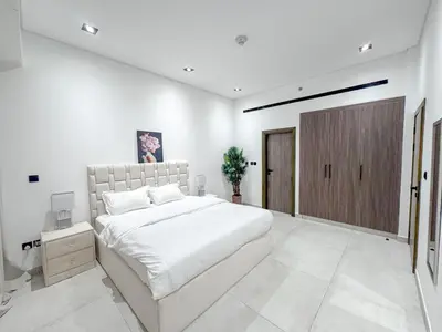 a white bedroom with a large bed and a wooden door at Chic 1BR Retreat with Infinity Pool and Sauna in JVC, Dubai in Dubai
