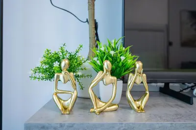three gold statues sitting on a table with flowers at Bright studio oplaz by Danube Near Miracle Garden in Dubai