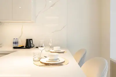 a white kitchen with a table with plates and glasses at PVH - Burj Khalifa View Studio - Emaar Residences in Dubai