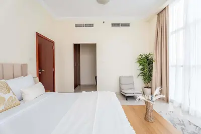 a white bedroom with a large bed and a chair at Chic 1BR w Pool Sauna & Steam Room Access in Dubai