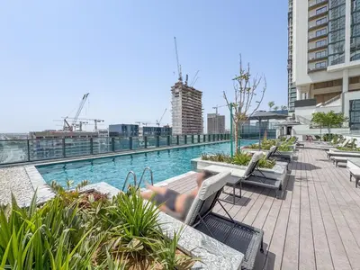a woman laying on a bench next to a swimming pool at Vogue Al Maktoum City Sobha Hartland The Crest Near to Downtown, Burj Khalifa and Dubai Mall, Three Bedroom plus Kid's room apartment with Balcony and City View, Access to all Amenities in Dubai