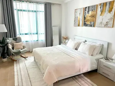 a white bedroom with a large bed and a chair at Cozy 1BR Stay in Dubai Marina Near Beach and Tram in Dubai
