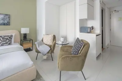 a bedroom with a bed and two chairs and a kitchen at Frank Porter - The Vogue, Business Bay in Dubai
