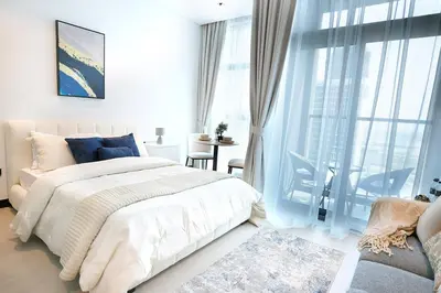 a white bedroom with a bed and a large window at Cozy Studio, All Bills Included in Dubai