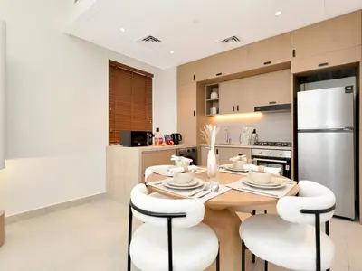a kitchen with a wooden table and white chairs at Elegant 2BR Apartment in Socio Tower - Dubai Hills in Dubai
