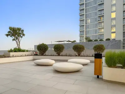 a courtyard with white chairs and a building at Spacious 1BR for 2, 10 Min Meydan Racecourse, Pool & Gym Access in Dubai