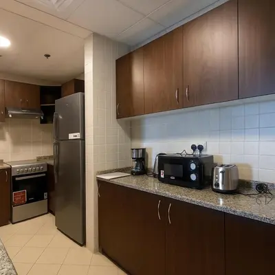 a kitchen with wooden cabinets and a black refrigerator at Sunset Beach Escape at Palm Jumeirah 2BR 241 by The Rosewood Vacation Homes Rental LLC in Dubai
