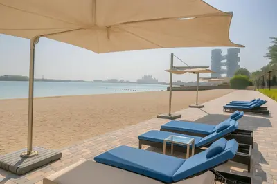 two blue lounge chairs and an umbrella on the beach at Sunset Beach Escape at Palm Jumeirah 2BR 241 by The Rosewood Vacation Homes Rental LLC in Dubai