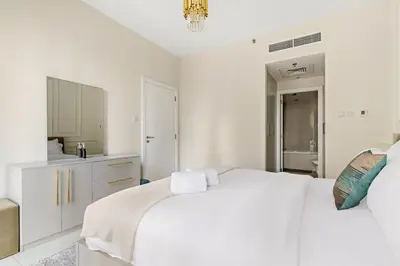 a white bedroom with a large white bed and a kitchen at FIRST CLASS 1BR Burj Khalifa View , Near Metro in Dubai