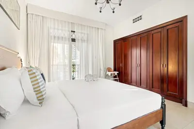 a bedroom with a large white bed and a wooden cabinet at FIRST CLASS 1BR Cozy Old Town Escape in Dubai