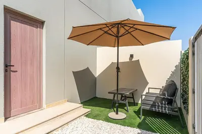 a patio with an umbrella and a table and a chair at Stylish 1BR Villa near Global Village and Golf Clubs in Dubai