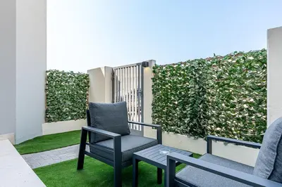 a balcony with two chairs and a green hedge at Stylish 1BR Villa near Global Village and Golf Clubs in Dubai