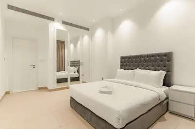 a white bedroom with a large bed and a mirror at FIRST CLASS 2BR Elegant Duplex Haven in Dubai