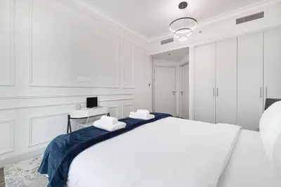 a white bedroom with a large bed and a desk at StayMada - Torch Tower Stunning Balcony City Views in Dubai