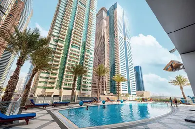 a swimming pool with palm trees and tall buildings at StayMada - Torch Tower Stunning Balcony City Views in Dubai