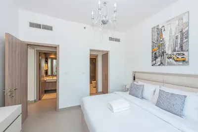 a white bedroom with a large bed and a chandelier at VayK - Brand New 1BR in Dubai Hills in Dubai