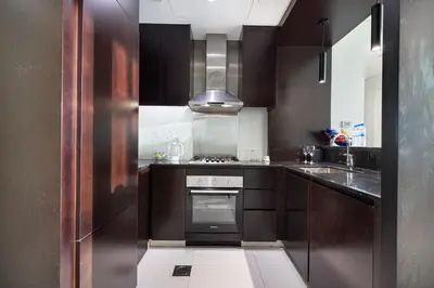 a kitchen with brown cabinets and a stove top oven at Maison Distinction Suites by Hostiva - Burj and Fountain View in Dubai