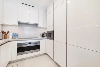 a white kitchen with stainless steel appliances and white cabinets at New Luxury Canalfront 2 Bedroom Apartment with Burj Views in Dubai