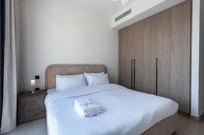 a bedroom with a white bed with a wooden cabinet at Modern Townhouse in Tilal Al Ghaf I Aura Gardens in Dubai