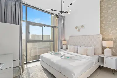 a white bedroom with a bed and a large window at Chic Living 1 bedroom near Dubai Hills Mall in Dubai