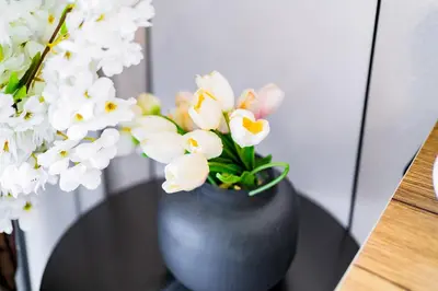 a black vase filled with white flowers on a table at Luxury Grande 48 with Burj Khalifa & Fountain Views in Dubai