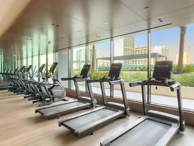 a row of treadmills in a gym with a large window at Modern 1BR Apartments by Nestovia in JVC with Pool and City Views in Dubai