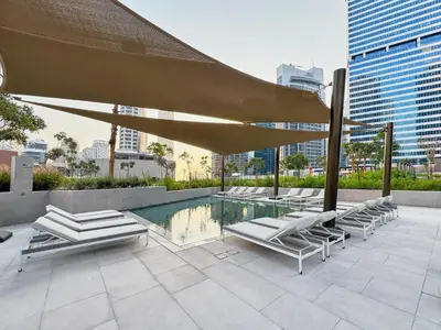 a pool with lounge chairs and a large umbrella at Modern Studio in Business Bay with Pool, Gym & Canal View in Dubai