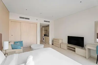 a white bedroom with a large bed and a flat screen tv at Stylish Studio with Rooftop Pool on the Palm in Dubai
