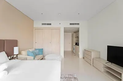 a white bedroom with a bed and a living room at Stylish Studio with Rooftop Pool on the Palm in Dubai