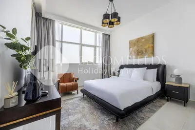 a white bedroom with a bed and a chair at Bloomfields Cozy Stu Damac Ghalia Jvc in Dubai