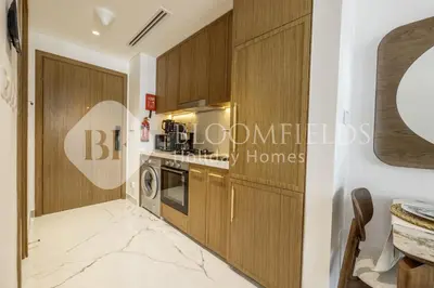 a kitchen with wooden cabinets and a washer and dryer at Bloomfields Lumière Stu Azizi Riviera in Dubai