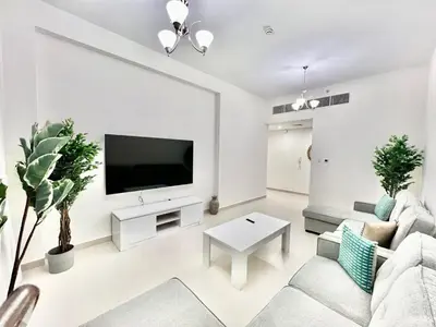 a white living room with a flat screen tv at Not far from metro Spacious in Dubai