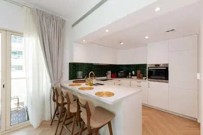 a kitchen with white cabinets and a kitchen island with chairs at Al Dhafrah 4, The Greens - Onelink in Dubai
