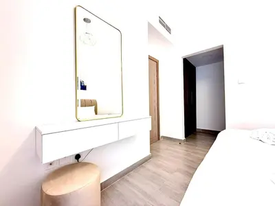 a white bedroom with a mirror and a stool at Majestic 2 BHK Park view at Liwan 2- Dubai in Dubai