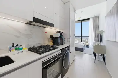 a white kitchen with a stove and a sink at Modern Studio on High Floor with Stunning City Views near Circle Mall and Community Parks - Binghatti Tulip, JVC - by Deluxe Holiday Homes in Dubai