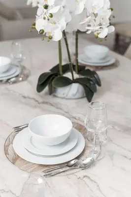 a table with plates and glasses and a vase with white flowers at PVH - Elegant 2BR near Dubai Mall - Opera Grand in Dubai