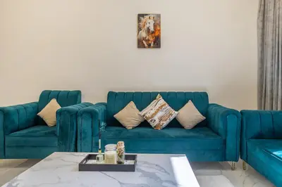 a living room with a blue couch with pillows at 1BR Poolside Serenity in JVT in Dubai