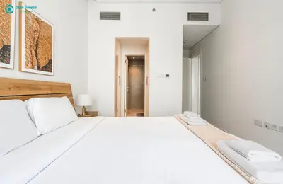 a white bedroom with a large white bed with a desk at Blue Breeze Modern 2BR Apartment Near Downtown in Dubai