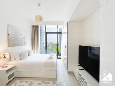 a white bedroom with a bed and a flat screen tv at Premium Riviera Studio King Bed, Pool & Gym in Dubai