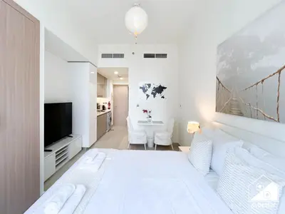 a white bedroom with a large bed and a tv at Premium Riviera Studio King Bed, Pool & Gym in Dubai