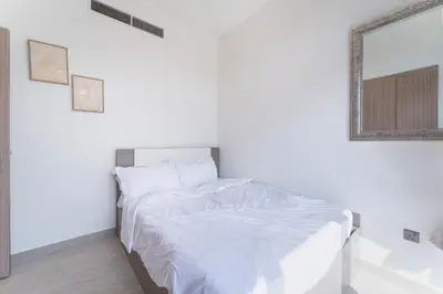 a white bedroom with a bed and a mirror at HAVN - Spacious 1 bedroom in Azizi Riviera, Meydan in Dubai