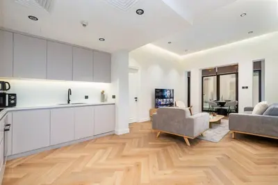 a kitchen with white cabinets and a living room at Newly Refurbished Luxury Garden Apartment with Burj Khalifa View and Direct Pool Access in Downtown Dubai in Dubai