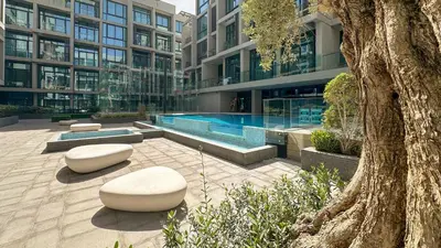 a building with a swimming pool and two white benches at Maison Privee - Serene Studio Escape with Balcony in JVC in Dubai