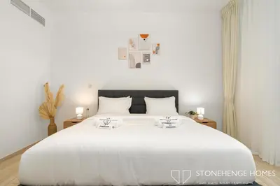 a white bedroom with a large white bed with two tables at Cozy 1BR in Belgravia , JVC, Pool View, 20 Min from Downtown Dubai in Dubai